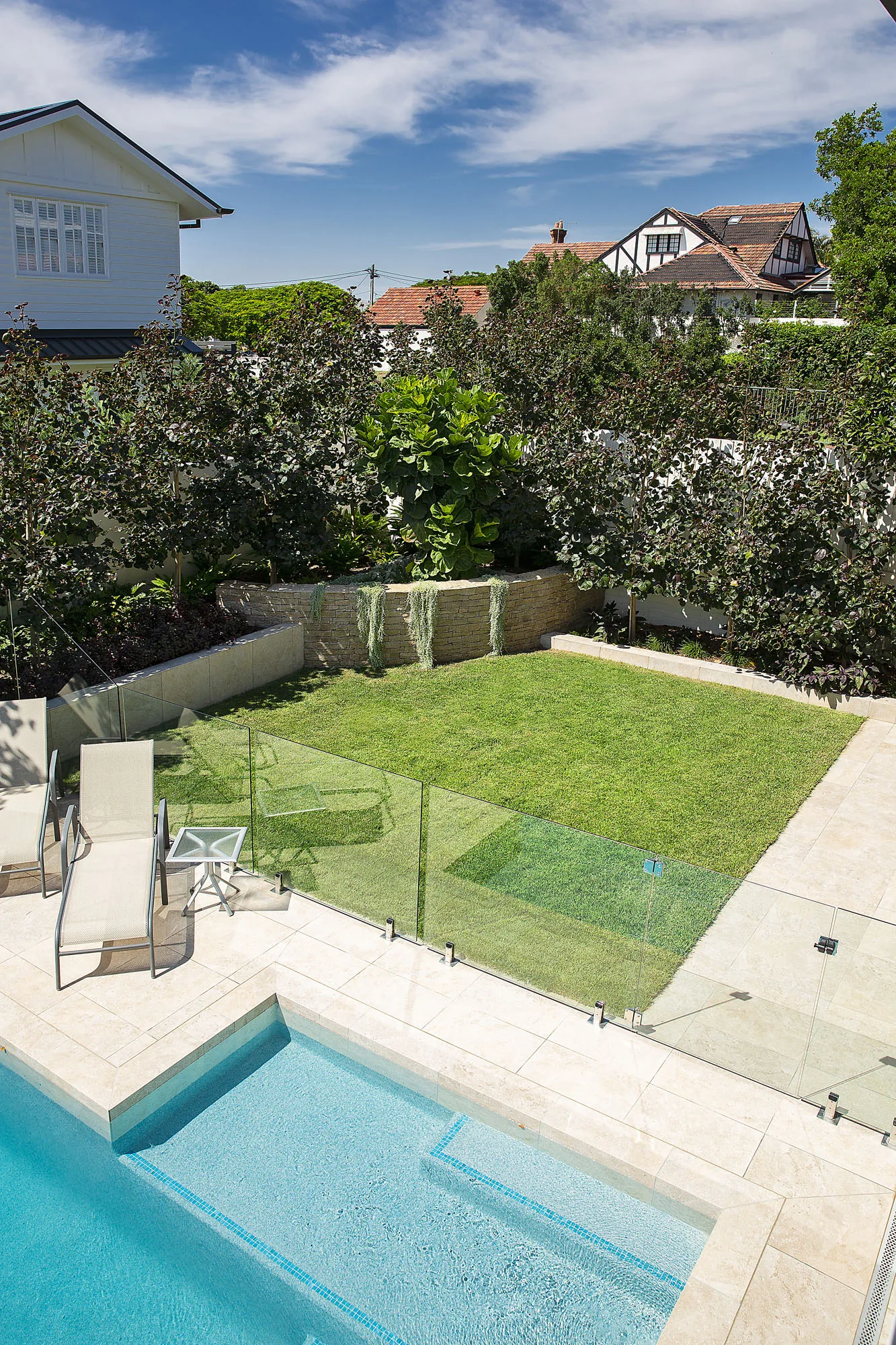 Compact plunge pool set into a lawn panel beside a rendered retaining wall and a single specimen tree