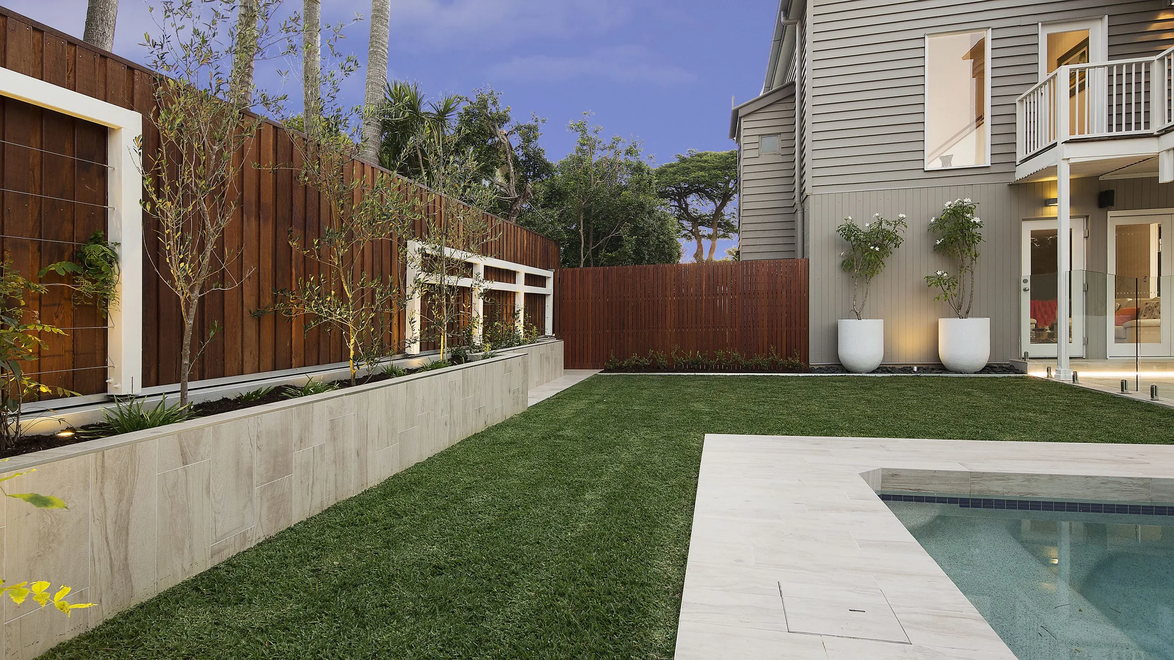 Small geometric pool set into a lawn panel beside a frameless glass fence and timber fence line