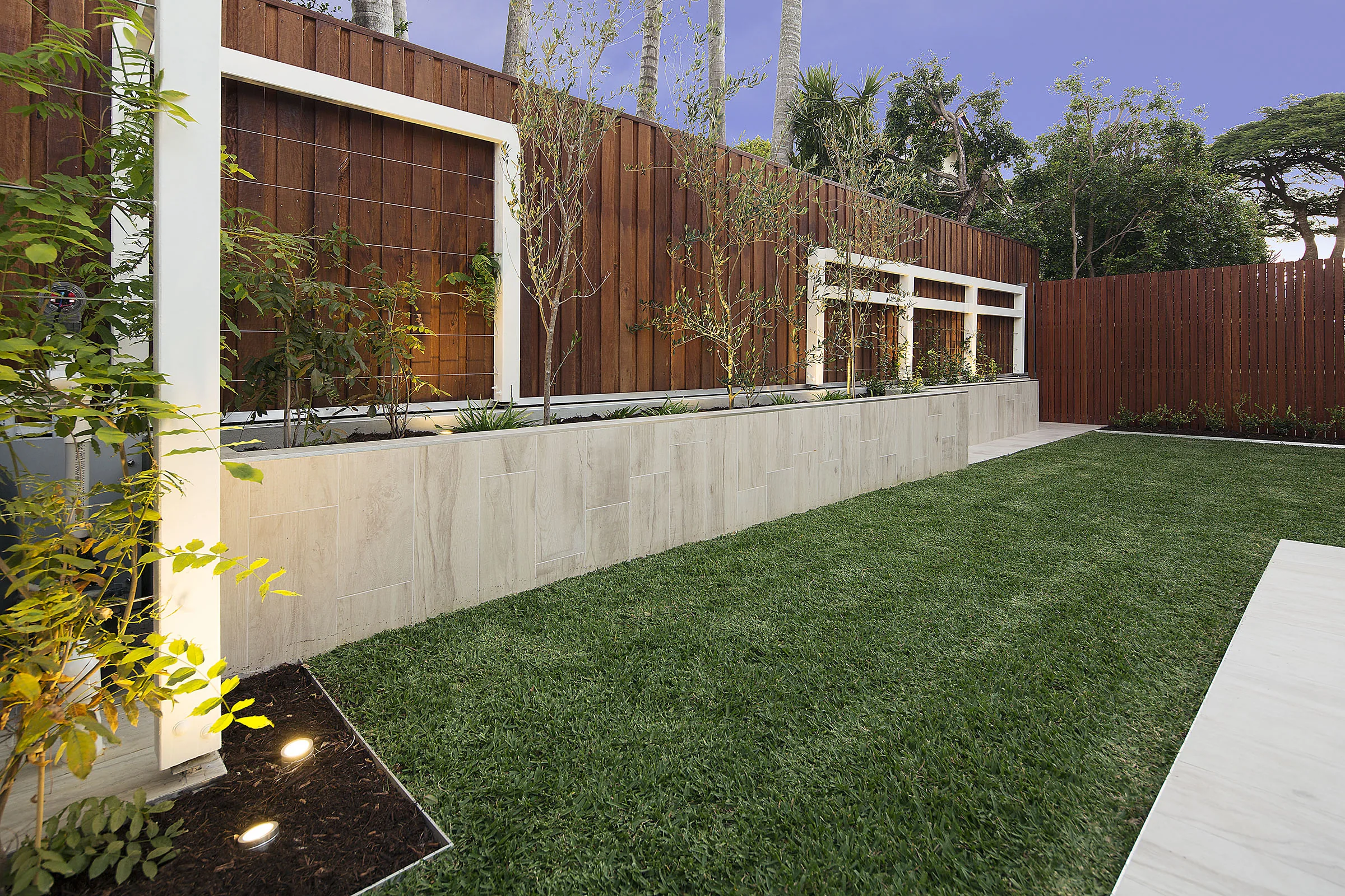 Triangular lawn panel bordered by a timber batten fence and a rendered stone-clad retaining wall