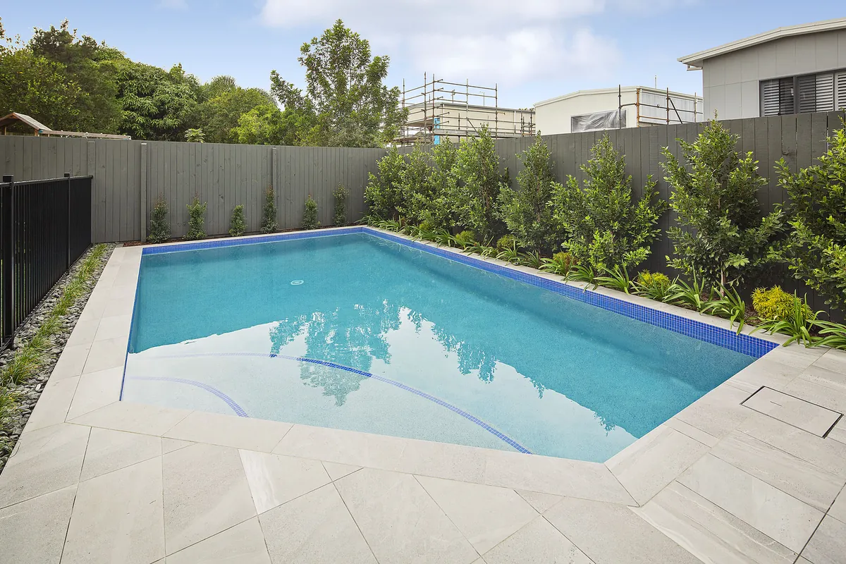 Diamond-shaped pool edged with native grasses and strappy planting along a dark timber paling fence