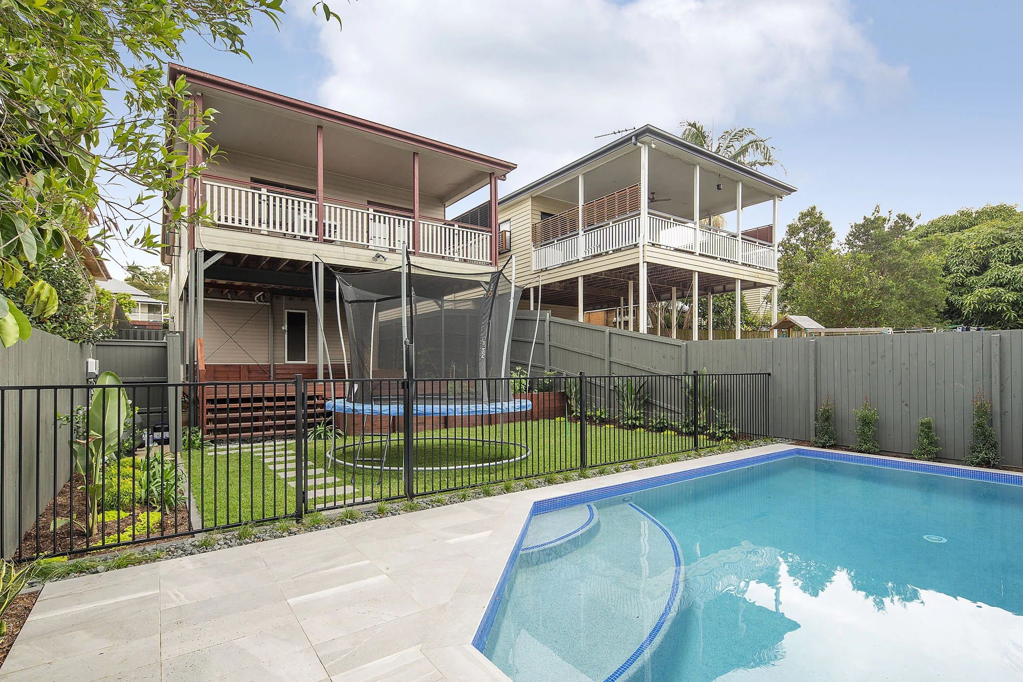 Rectangular pool beside a traditional two-storey timber home with a black steel boundary fence