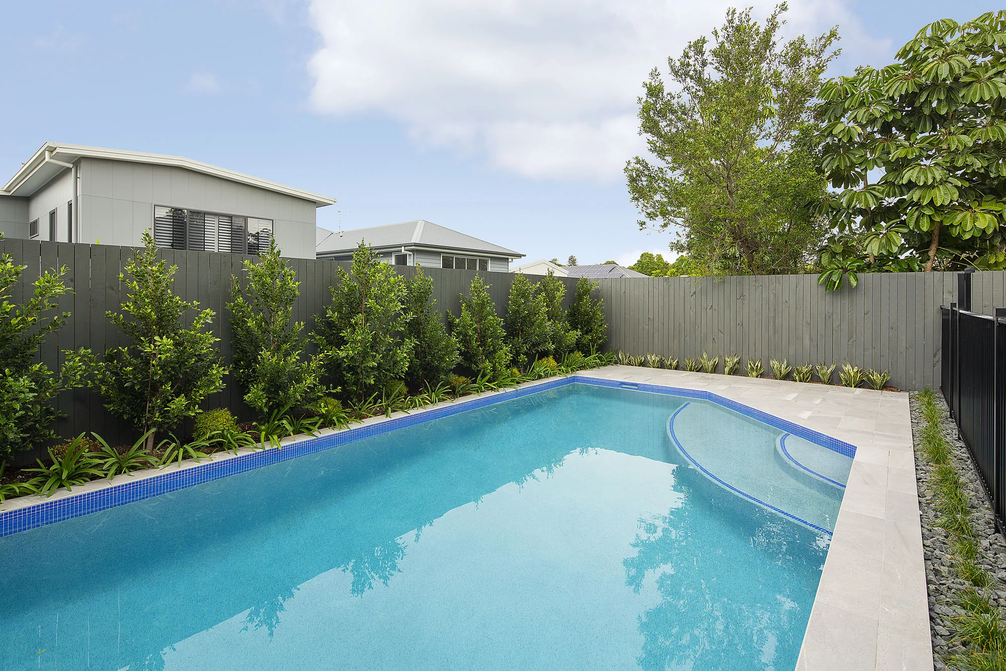 Rectangular pool with blue waterline tile bordered by a clipped hedge screen