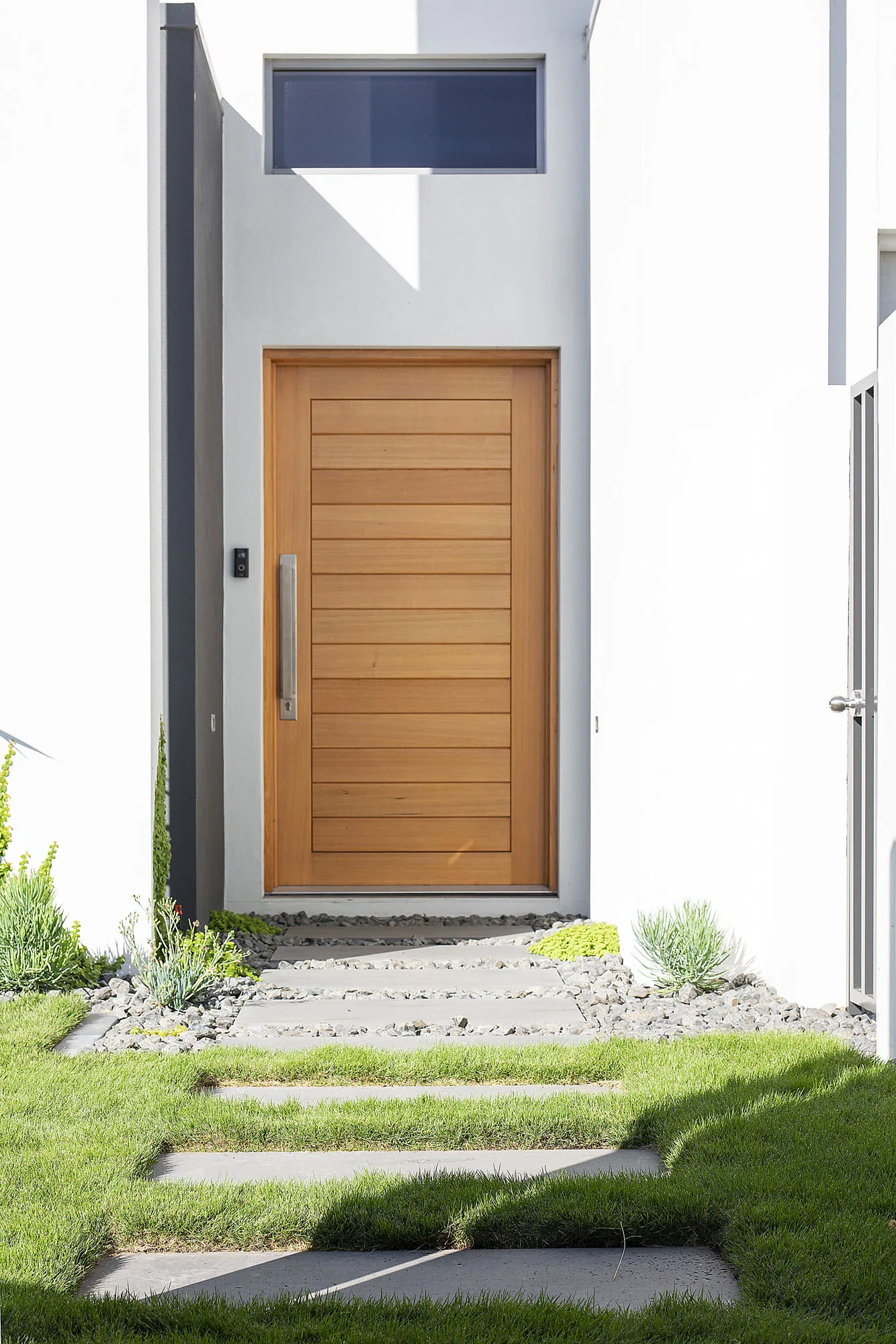 Timber entry door and stepping pavers through a narrow side garden with native planting