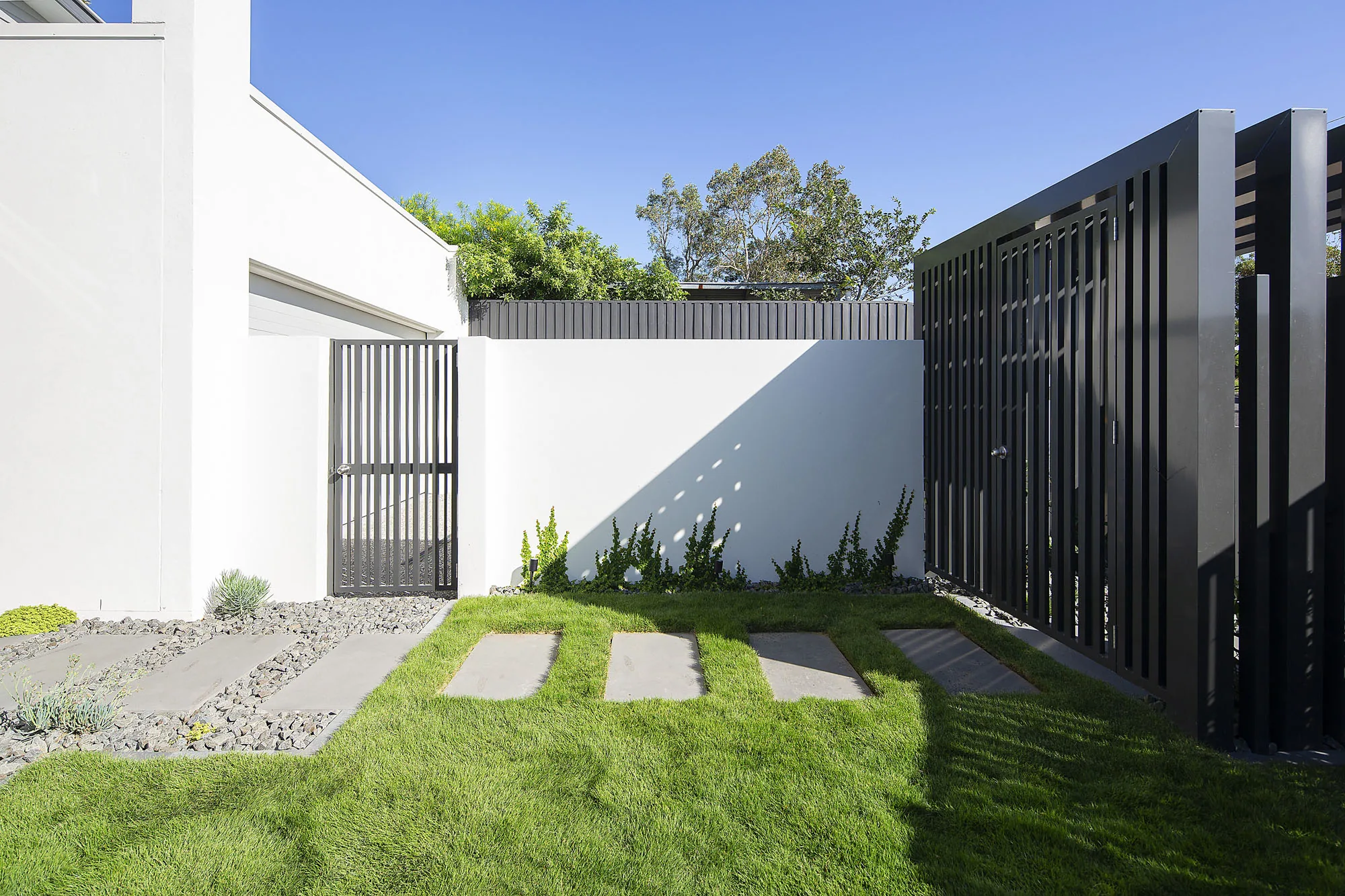 Small courtyard with black steel privacy screening, pavers, and lawn against a rendered wall