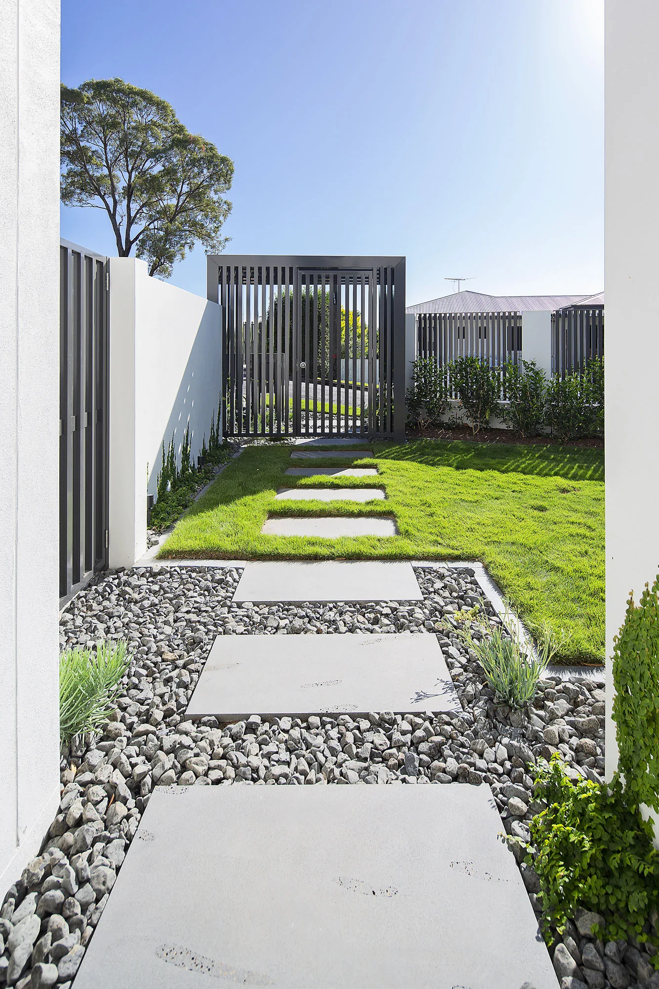 Narrow paved side path leading to a steel gate between rendered boundary walls