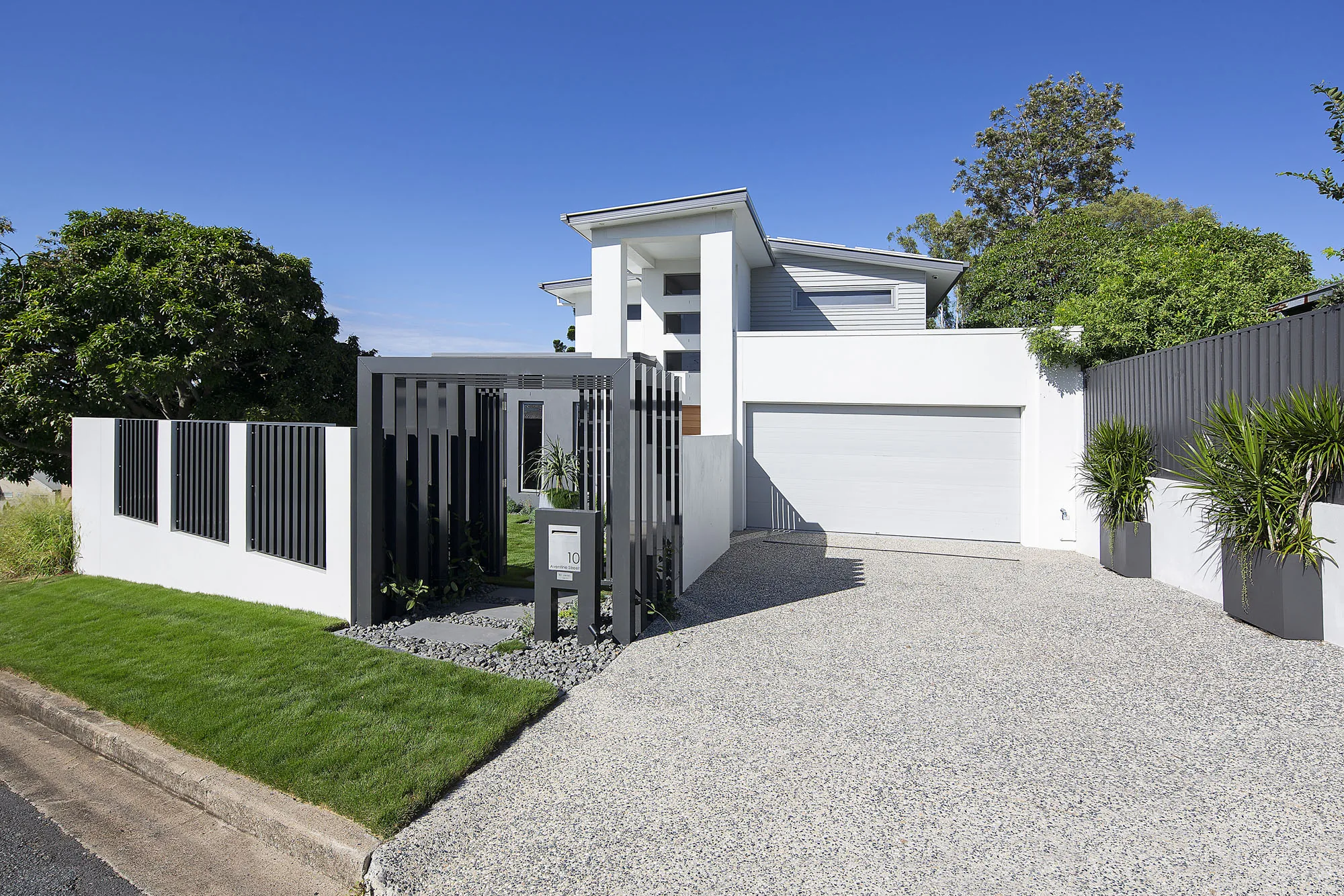 Street view of a contemporary black-clad home with a steel entry gate and clipped lawn