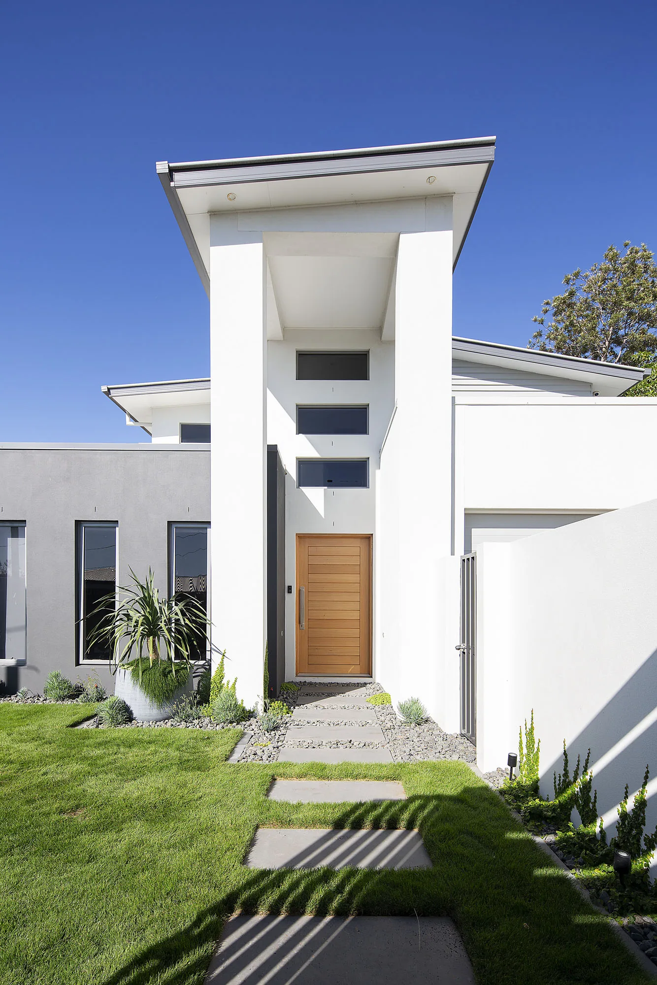 Street facade of a white rendered contemporary home with a timber entry door