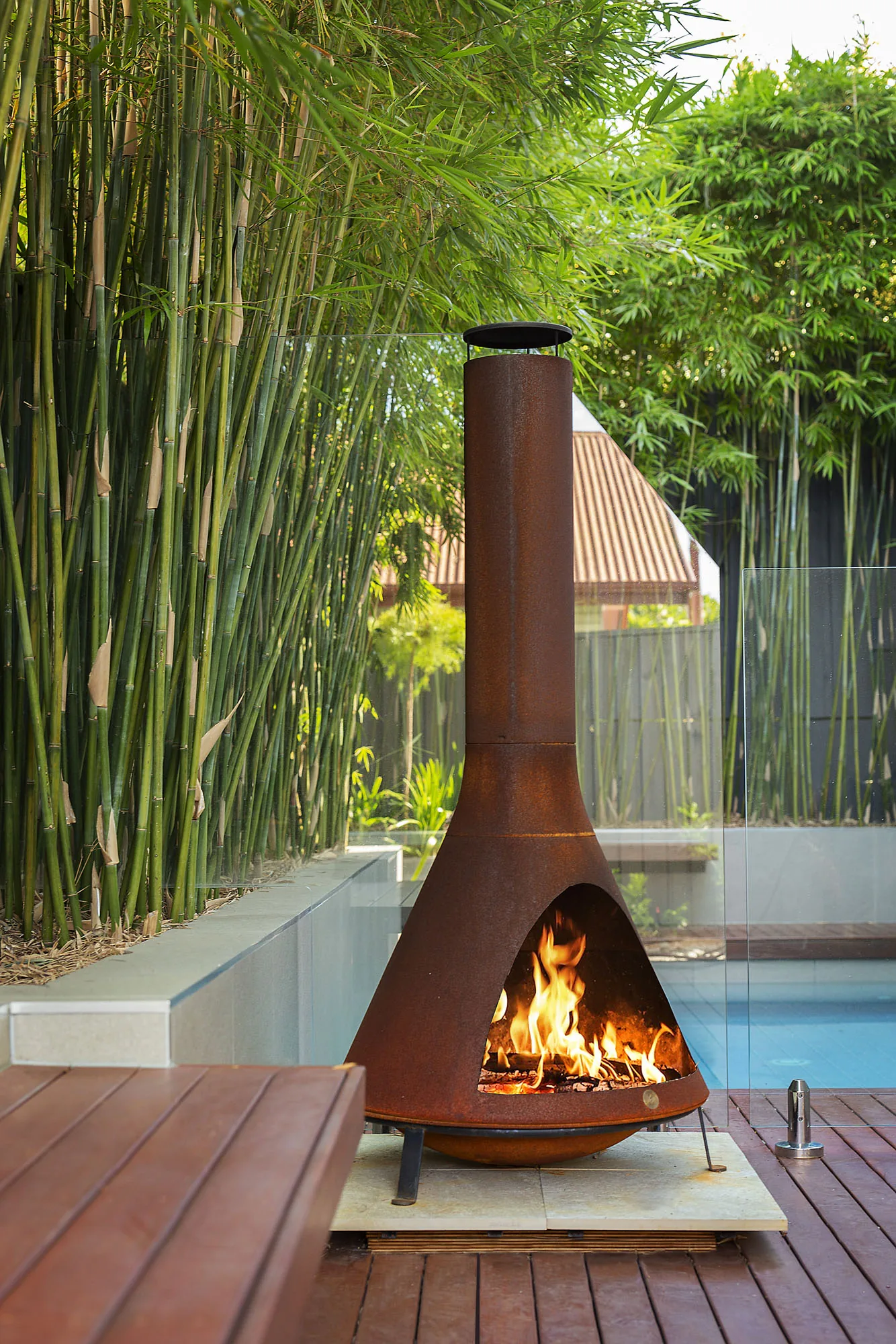 Corten steel fireplace detail on a timber deck against a bamboo privacy screen
