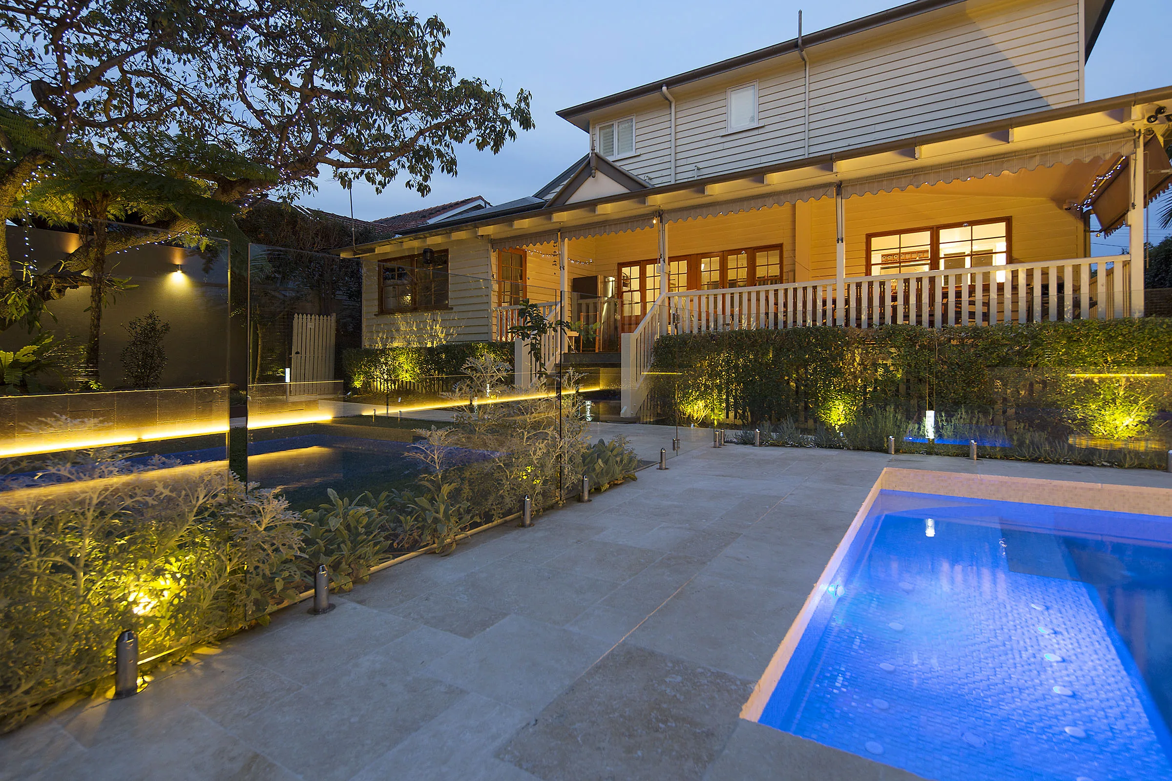 Rectangular pool at dusk framed by a rendered boundary wall and glass pool fencing