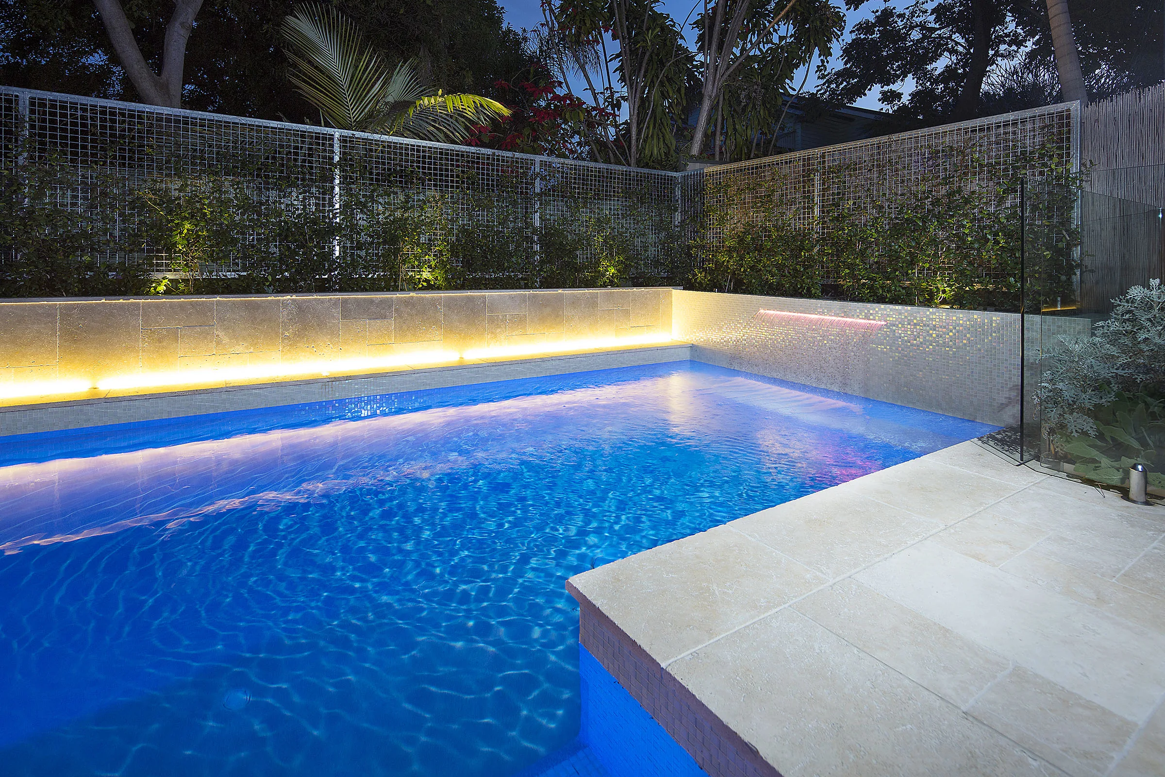 Close view of a rectangular pool corner at night with glowing waterline lighting