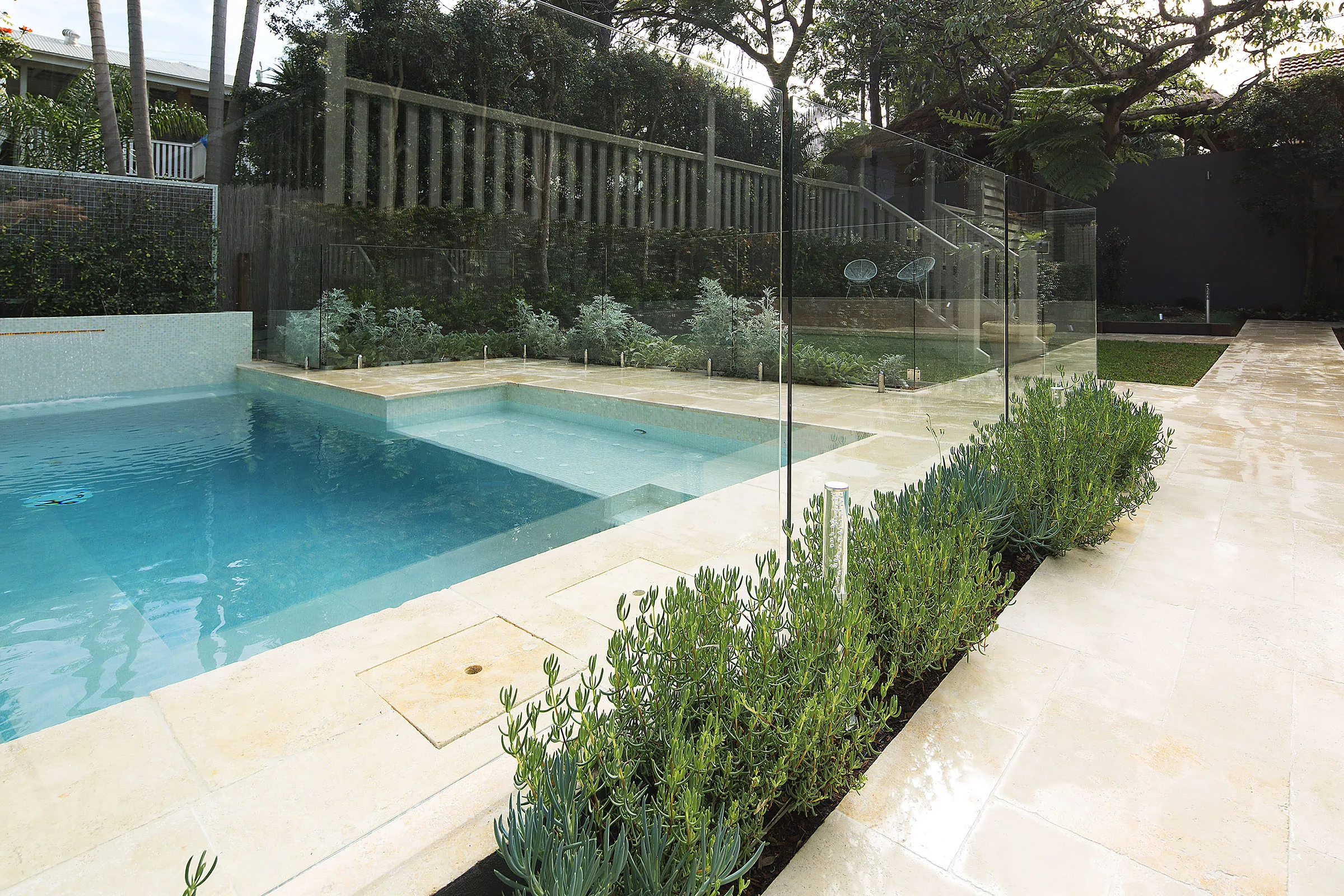 Rectangular pool with clipped hedge boundary and travertine coping in daylight