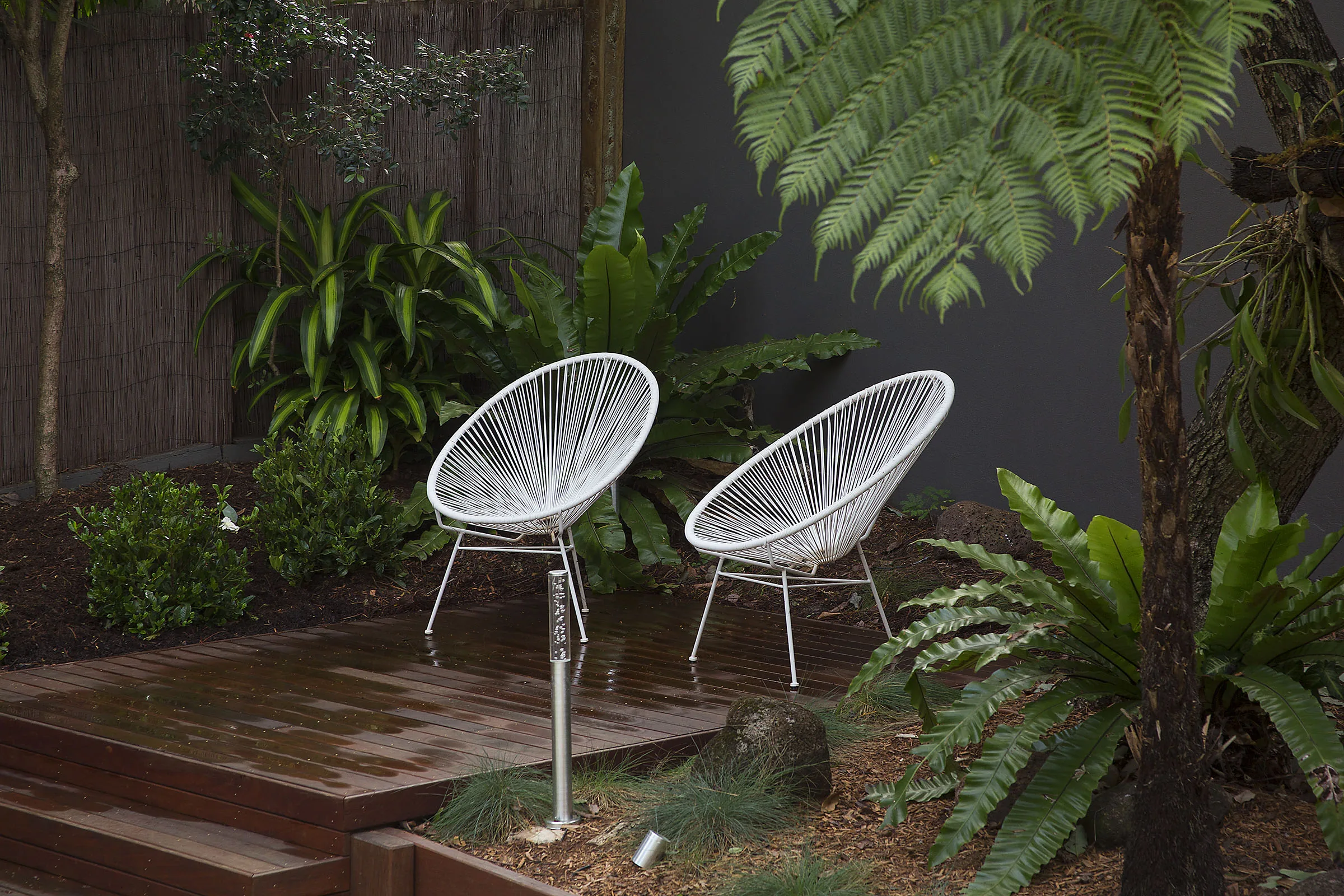 Pair of outdoor chairs on a travertine terrace shaded by mature trees and ferns