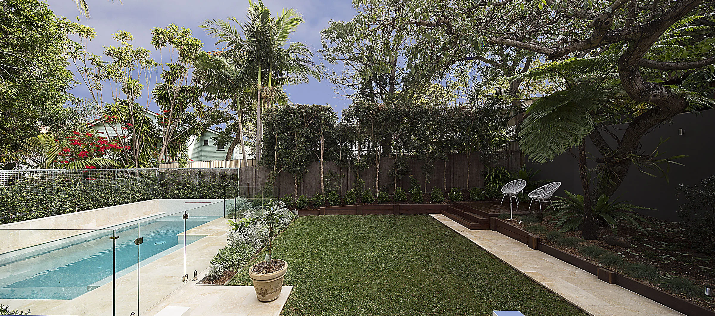 Full width view of a manicured lawn and rectangular pool with glass fencing