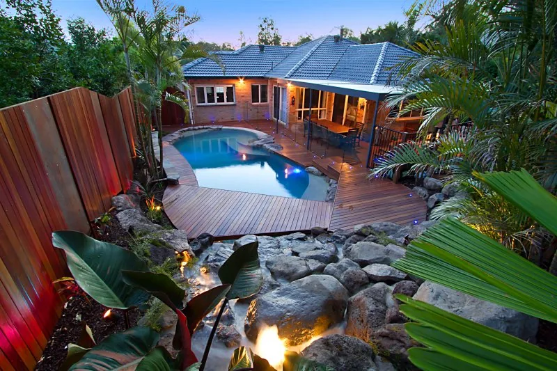 Aerial view over giant banana leaves and palm fronds down to a free-form pool and timber deck at dusk
