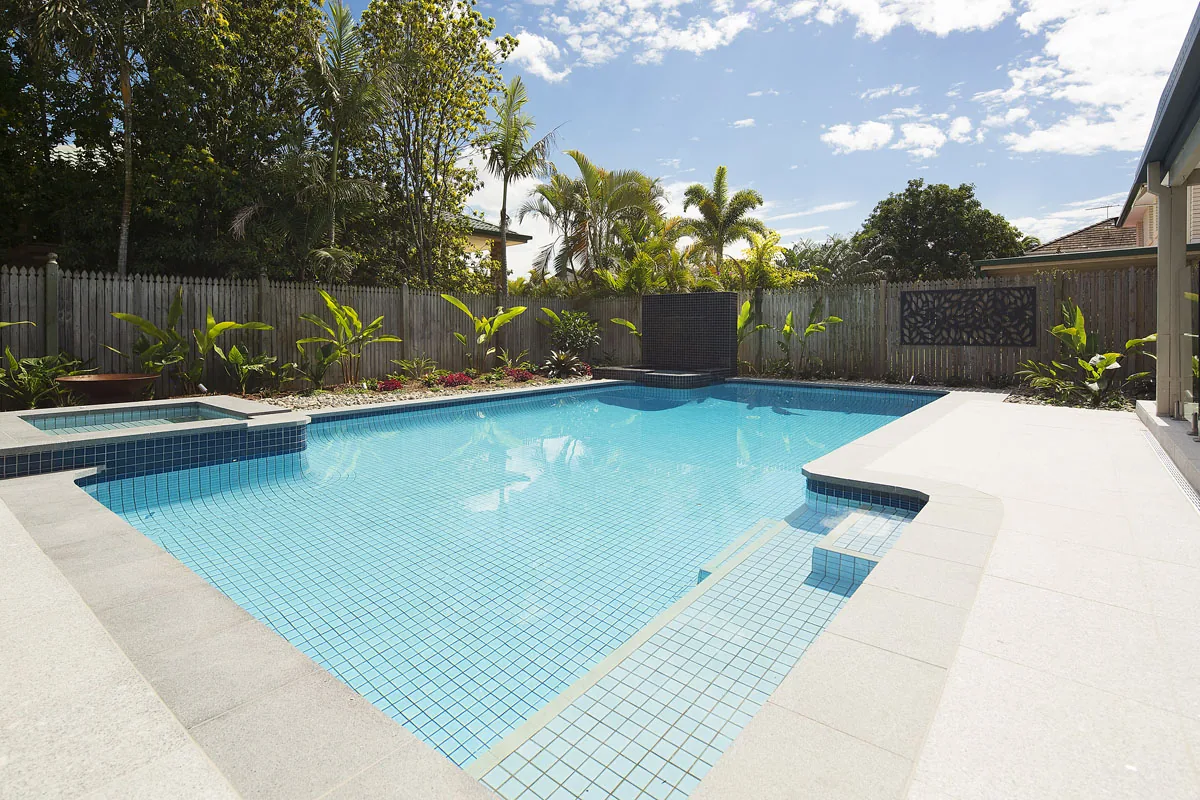 Rectangular pool with a dark-tiled spa inset and travertine coping backed by tropical planting