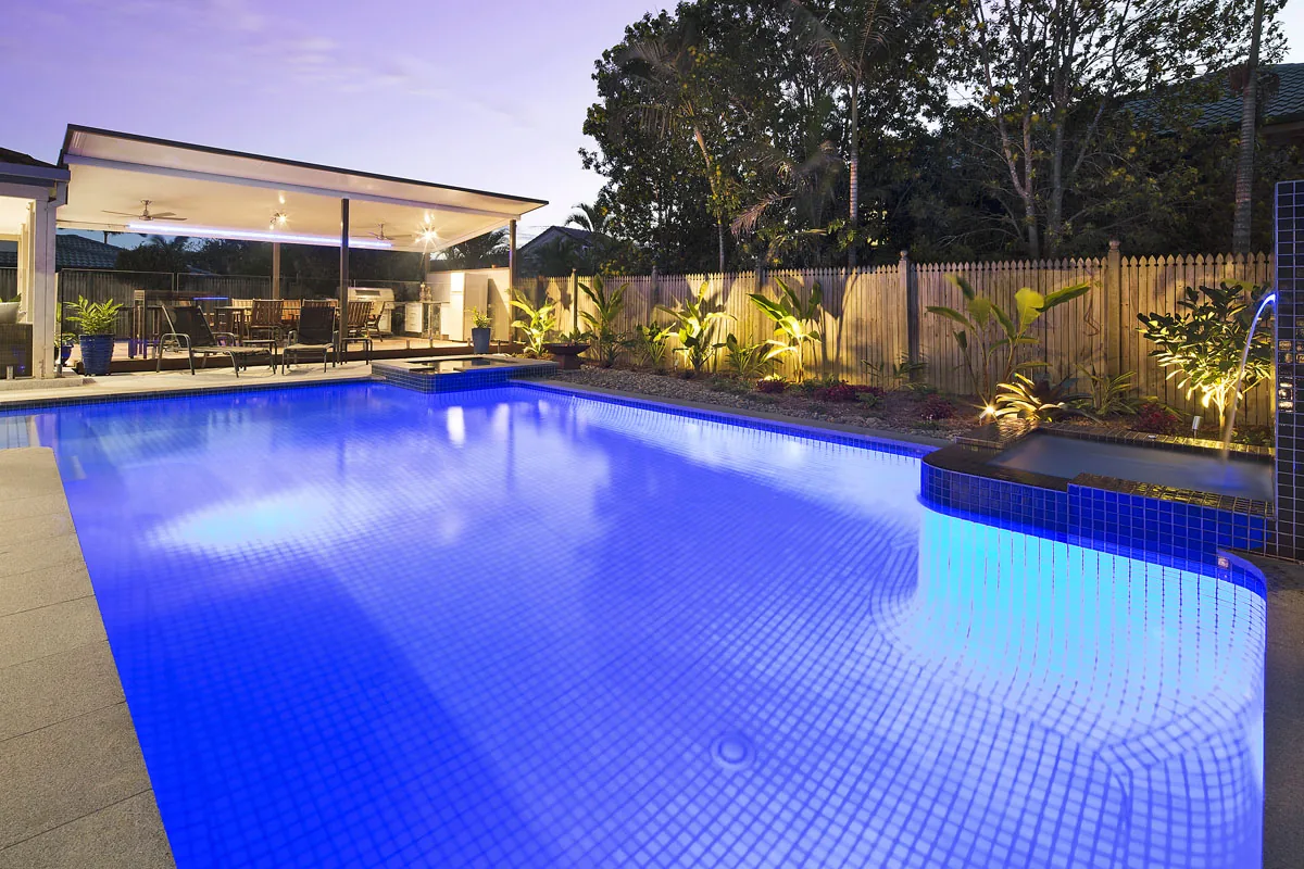 Pool at night lit with blue underwater lighting against a dark timber fence