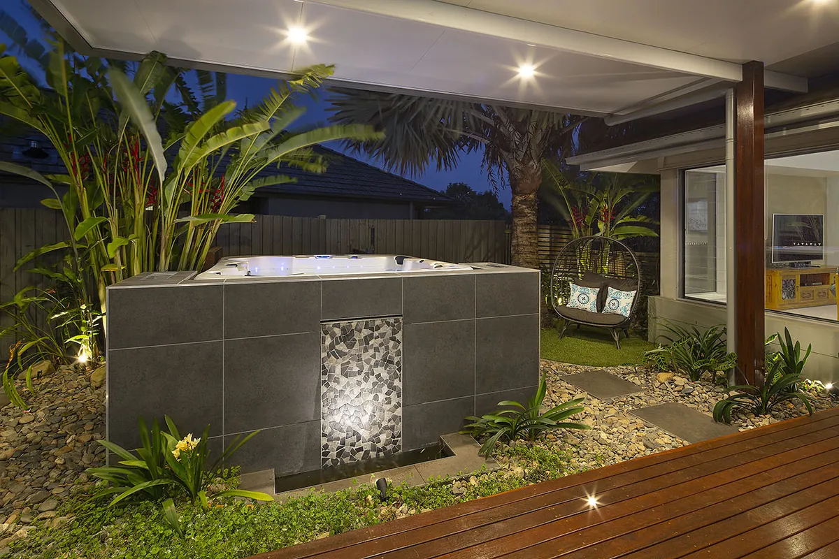 Tiled spa with a pebble mosaic water feature and a woven egg chair nook framed by tropical banana and heliconia planting at dusk