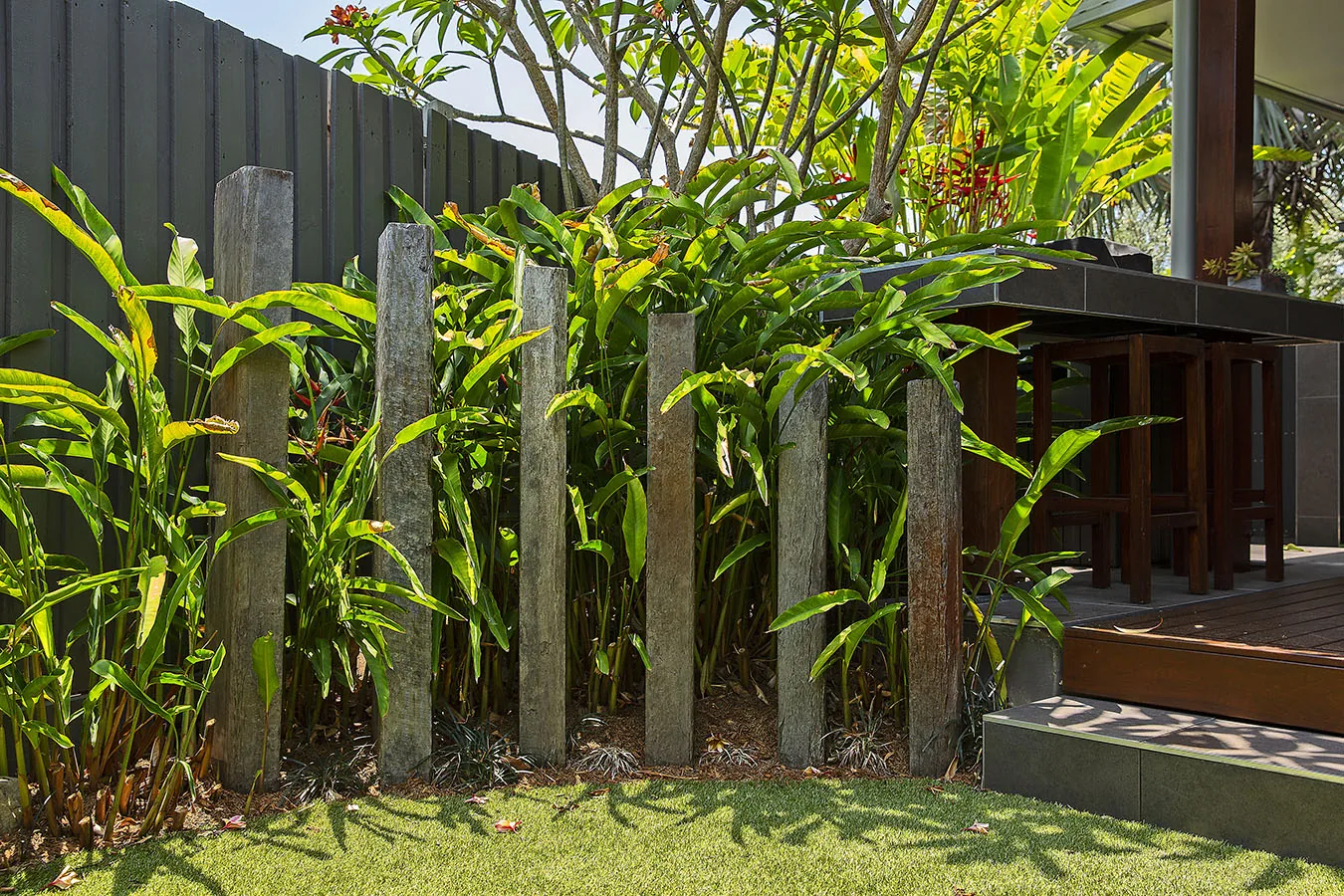 Timber bar table and stools tucked beneath tropical palms and a frangipani tree