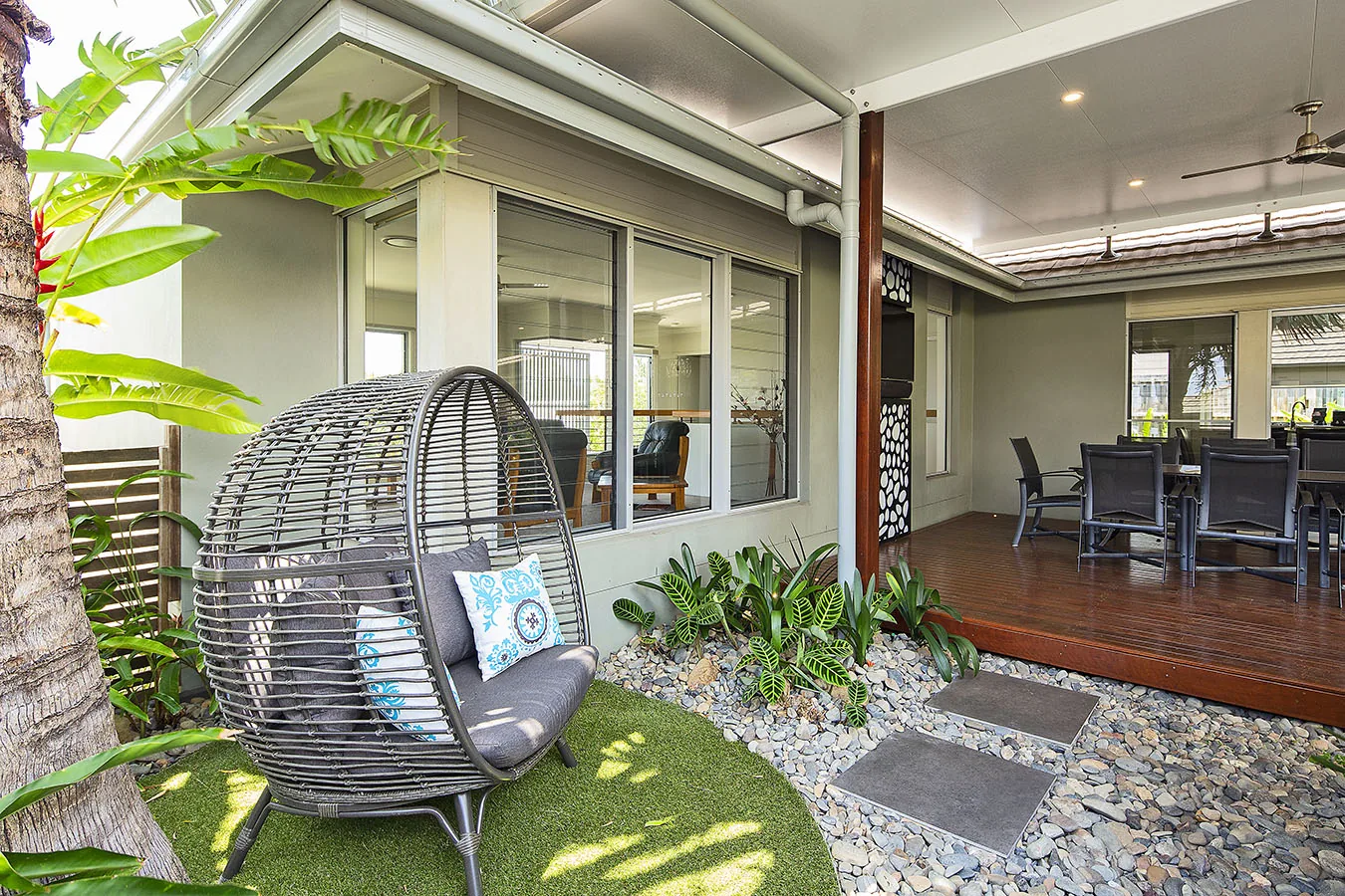 Woven egg chair nook set among tropical planting beside a gravel path