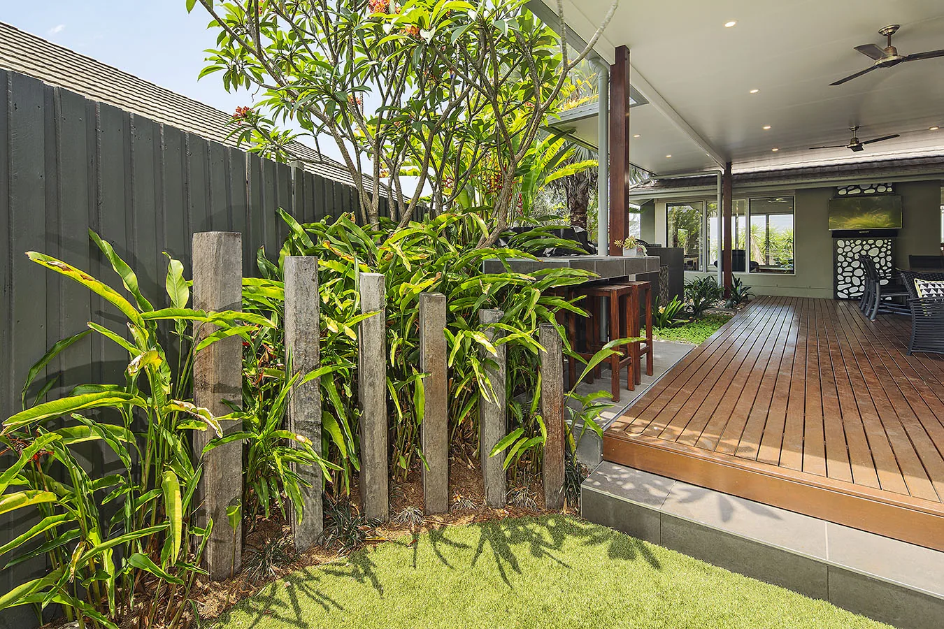 Flowering frangipani and heliconia planting massed around timber sleeper posts beside an outdoor kitchen deck